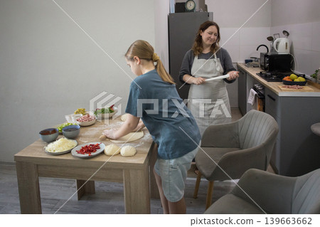 Happy mother and daughter cooking italian pizza together in cozy home kitchen. Happy mother and daughter cooking italian pizza together in cozy home kitchen. 139663662