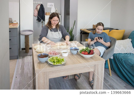 Happy mother preparing pizza and daughter using smartphone gadget at home Happy mother preparing pizza and daughter using smartphone gadget at home 139663666