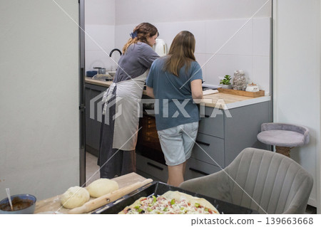 Mature mother and daughter cooking italian pizza together in cozy home kitchen. Mature mother and daughter cooking italian pizza together in cozy home kitchen. 139663668