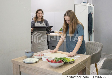 Nice daughter and mother cooking italian pizza together in cozy domestic kitchen. Nice daughter and mother cooking italian pizza together in cozy domestic kitchen. 139663669