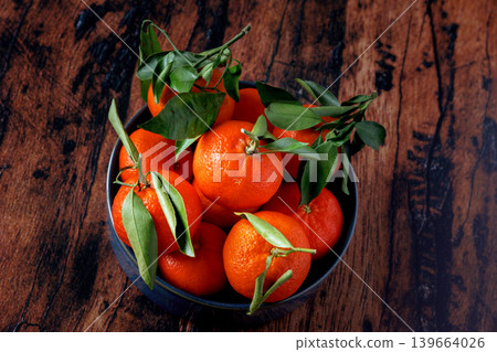 Clementines with leaves in a blue ceramic dish on an old wooden table Clementines with leaves in a blue ceramic dish on an old wooden table 139664026