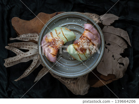 Two delicate, crescent-shaped rolls bun blushing with pastel hues of lavender and jade rest elegantly on a rustic ceramic plate, drizzled with a savory chili paste glaze and crowned with a fine Two delicate, crescent-shaped rolls bun blushing with pastel hues of lavender and jade rest elegantly on a rustic ceramic plate, drizzled with a savory chili paste glaze and crowned with a fine 139664206