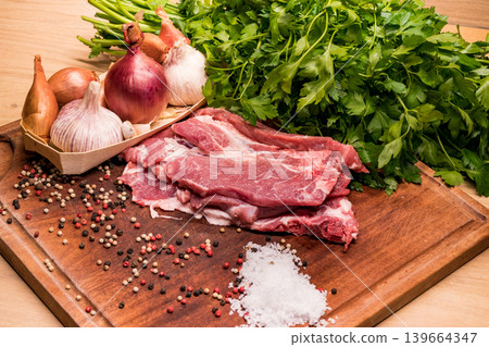 Raw pork meat with garlic, onions, parsley and spices on wooden board Raw pork meat with garlic, onions, parsley and spices on wooden board 139664347