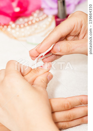 The esthetician removes the old nail polish with a cotton and remover The esthetician removes the old nail polish with a cotton and remover 139664350