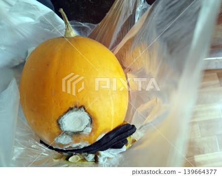 Bright orange pumpkin sits inside a transparent plastic bag, showing a large, circular patch of white and grey mold on its side. This image captures the natural process of food decay and spoilage 139664377