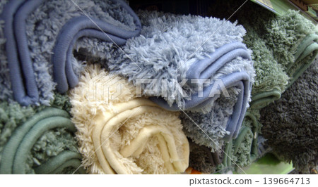 Soft, shaggy bath mats in various colors like blue, cream, and green are neatly folded on a store shelf. The thick, plush texture of the microfiber fabric is visible in this close-up retail shot Soft, shaggy bath mats in various colors like blue, cream, and green are neatly folded on a store shelf. The thick, plush texture of the microfiber fabric is visible in this close-up retail shot 139664713