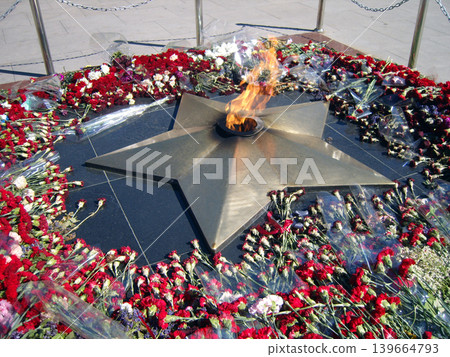 An eternal flame burns from a bronze star-shaped monument, surrounded by fresh red and white carnations. This powerful memorial honors fallen soldiers and signifies enduring national remembrance 139664793