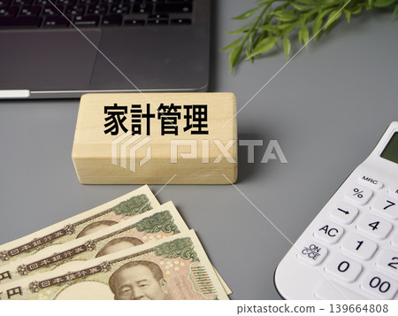 Simple financial elements featuring wooden blocks, a calculator, and banknotes, reminiscent of household budgeting, against a gray background. Simple financial elements featuring wooden blocks, a calculator, and banknotes, reminiscent of household budgeting, against a gray background. 139664808
