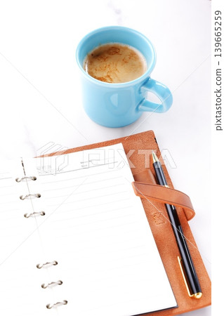 Image of a man working at his desk with a brown leather organizer while drinking a cafe latte, a coffee with milk 139665259