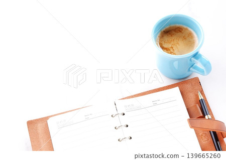 Image of a man working at his desk with a brown leather organizer while drinking a cafe latte, a coffee with milk Image of a man working at his desk with a brown leather organizer while drinking a cafe latte, a coffee with milk 139665260