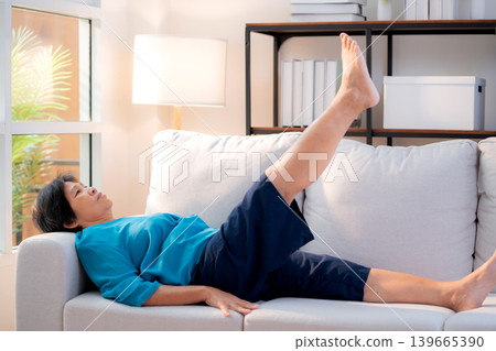 Senior asian woman practice stretch leg for treatment knee pain lying on sofa in living room. Senior asian woman practice stretch leg for treatment knee pain lying on sofa in living room. 139665390