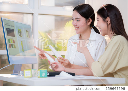 Two asian woman discussing cosmetic tube packaging sitting at modern home office. 139665396
