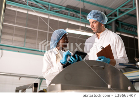 Diverse factory team workers inspecting large metal tank. Diverse factory team workers inspecting large metal tank. 139665407