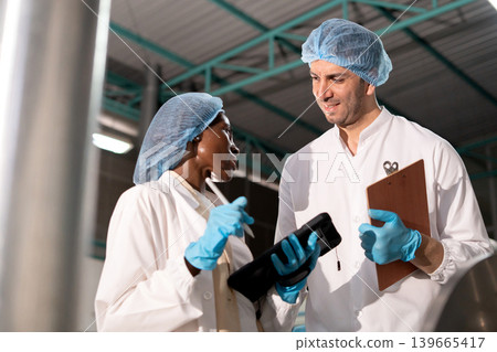 Diverse factory team workers inspecting large metal tank. Diverse factory team workers inspecting large metal tank. 139665417