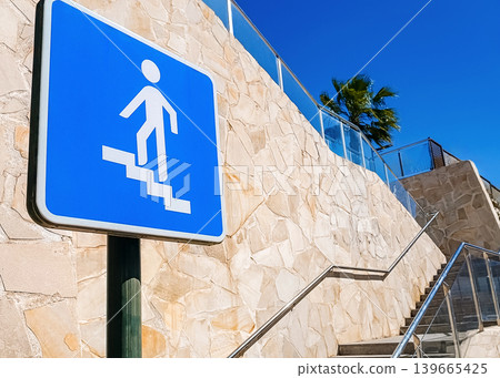 Pedestrian Stairway Sign Next to Modern Stone Wall Under Blue Sky Pedestrian Stairway Sign Next to Modern Stone Wall Under Blue Sky 139665425
