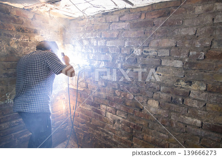 Welder working in dimly lit room with brick walls Welder working in dimly lit room with brick walls 139666273
