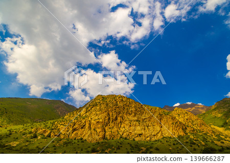 Jagged mountain face with green slopes and blue sky Jagged mountain face with green slopes and blue sky 139666287