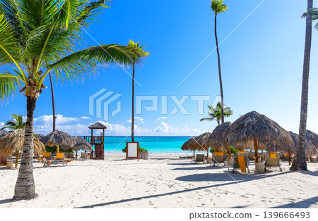 Tropical resort beach with palm trees, umbrellas and lounge chairs on white sand and turquoise ocean in Punta Cana, Dominican Republic. Tropical resort beach with palm trees, umbrellas and lounge chairs on white sand and turquoise ocean in Punta Cana, Dominican Republic. 139666493
