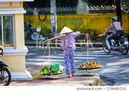 Traditional Vietnamese street vendor carrying baskets with tropical fruits in Ho Chi Minh City, Vietnam. 139666516