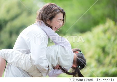 A smiling little girl hugs her mother in a park surrounded by fresh greenery. A picture of mother-daughter love and happy family time. "I love you, Mommy!" Mother's Day and a happy image. A smiling little girl hugs her mother in a park surrounded by fresh greenery. A picture of mother-daughter love and happy family time. "I love you, Mommy!" Mother's Day and a happy image. 139666813