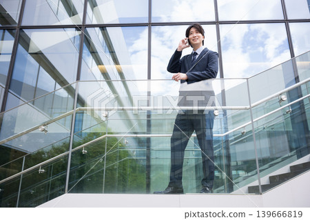 A businessman answering the phone on an outdoor staircase of a building – a full-body depiction of a sales scene showcasing speed, decisiveness, and judgment. A businessman answering the phone on an outdoor staircase of a building – a full-body depiction of a sales scene showcasing speed, decisiveness, and judgment. 139666819