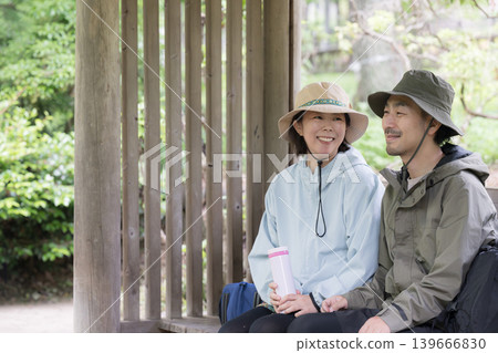 一對四十多歲的夫婦在山間涼亭或公園裡享受休息和交談;這是休閒和郊遊的畫面。 一對四十多歲的夫婦在山間涼亭或公園裡享受休息和交談;這是休閒和郊遊的畫面。 139666830