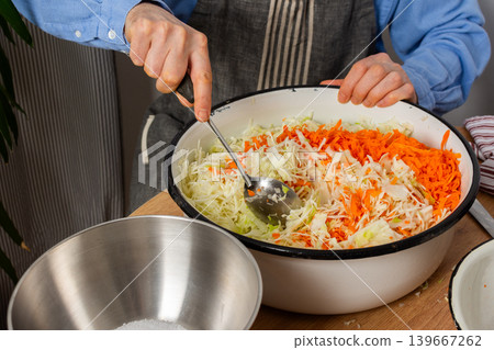 A 53-year-old man mixes cabbage and carrots in a large bowl in his kitchen while preparing for fermentation using simple tools and ingredients A 53-year-old man mixes cabbage and carrots in a large bowl in his kitchen while preparing for fermentation using simple tools and ingredients 139667262