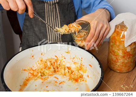 In a kitchen, a 53-year-old man works on fermenting cabbage and carrots. He carefully transfers the mixture into a glass jar for storage and fermentation In a kitchen, a 53-year-old man works on fermenting cabbage and carrots. He carefully transfers the mixture into a glass jar for storage and fermentation 139667264