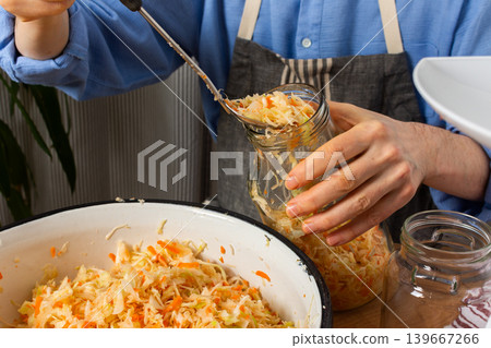 A 53-year-old man works in his kitchen fermenting cabbage and carrots. He carefully adds the mixture from a large bowl into a jar, showing concentration 139667266