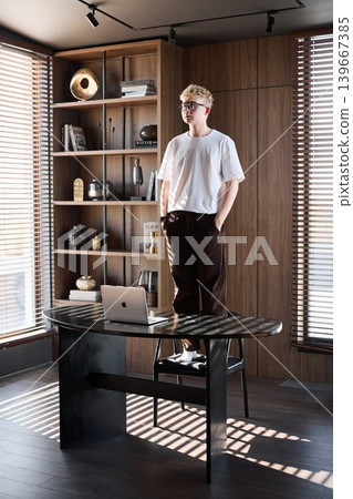 Young individual seated beside desk enjoying tranquil sunlight ambiance Young individual seated beside desk enjoying tranquil sunlight ambiance 139667385
