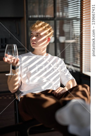 Serene young man lounging in warm afternoon shadows with glass of wine Serene young man lounging in warm afternoon shadows with glass of wine 139667431