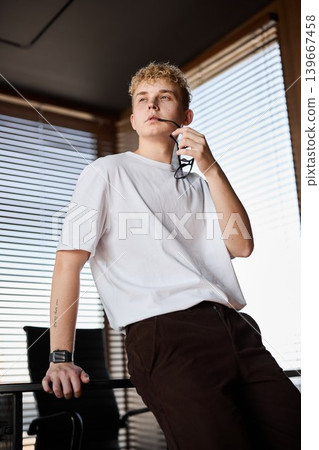Buoyant young guy casually holding coffee by bright window Buoyant young guy casually holding coffee by bright window 139667458