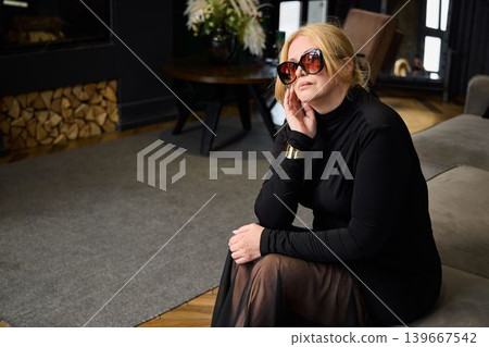 Chic white woman sitting comfortably near warm fireplace Chic white woman sitting comfortably near warm fireplace 139667542