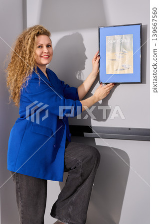 Woman stands confidently on ladder holding artwork in stylish room Woman stands confidently on ladder holding artwork in stylish room 139667560