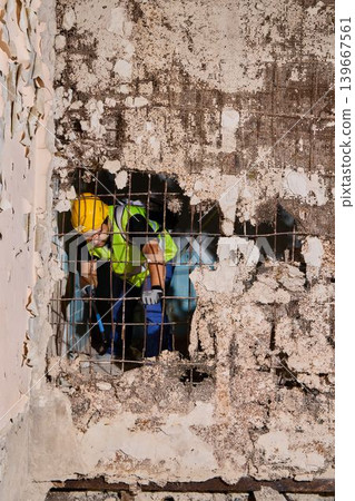Renovation crew coordinating repair through wall breach Renovation crew coordinating repair through wall breach 139667561