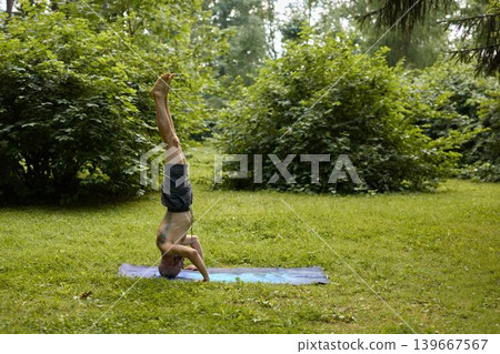 Individual maintains headstand position amidst vibrant park surroundings 139667567