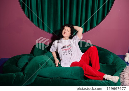 Reclining woman with red trousers against emerald setting Reclining woman with red trousers against emerald setting 139667677