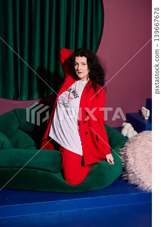 Woman in red suit seated on lush green setting with lively pose 139667678