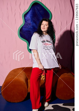 Casual woman leans against bright orange sofa in relaxed setting Casual woman leans against bright orange sofa in relaxed setting 139667683