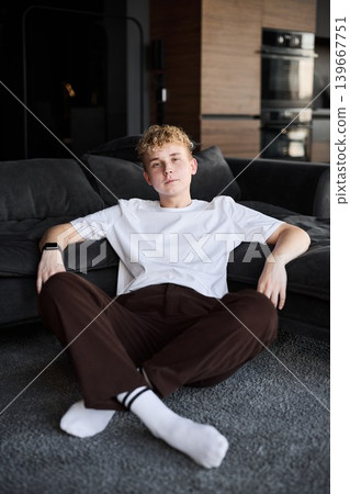 Adolescent seated on floor with contemplative gaze inside home 139667751