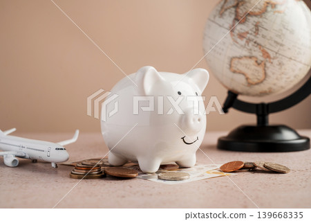 Hand putting coin into piggy bank with airplane and globe, travel savings budget planning and vacation finance concept 139668335