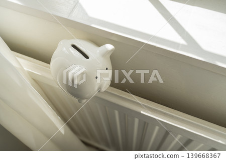 Piggy bank on home radiator, household energy savings heating costs and utility budget concept Piggy bank on home radiator, household energy savings heating costs and utility budget concept 139668367