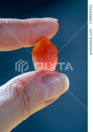 Food supplements. Female hand holding one vitamin jelly gummy strawberry shaped against dark background Food supplements. Female hand holding one vitamin jelly gummy strawberry shaped against dark background 139668401