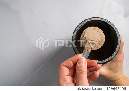 Chocolate whey protein powder in scoop, food supplements, female hand holding protein powder Chocolate whey protein powder in scoop, food supplements, female hand holding protein powder 139668406
