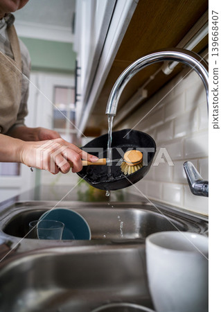 Woman washing a frying pan in the kitchen with eco friendly wooden brush for sustainable lifestyle Woman washing a frying pan in the kitchen with eco friendly wooden brush for sustainable lifestyle 139668407