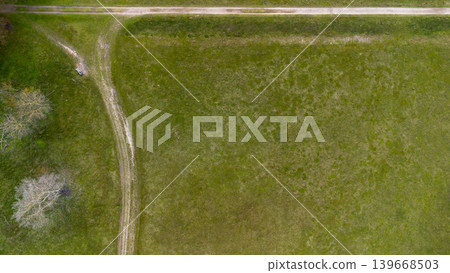 Top down aerial view of a green meadow with a dirt path intersection and a lonely bench. Minimalist rural landscape captured from above, showcasing texture, geometry, and peaceful countryside. Top down aerial view of a green meadow with a dirt path intersection and a lonely bench. Minimalist rural landscape captured from above, showcasing texture, geometry, and peaceful countryside. 139668503