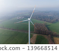 Aerial perspective of multiple wind turbines stretching into a misty, agricultural landscape on a clear, high-altitude morning. Sustainable green energy farm concept. 139668514