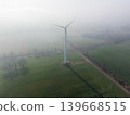 Aerial view of a solitary wind turbine standing in vast green agricultural fields on a foggy, misty morning. Clean energy technology in a rural environment. 139668515