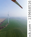 Aerial view looking through the rotating blade of a wind turbine, showing a single turbine standing in a misty, agricultural landscape. Sustainable green energy concept in fog. 139668516