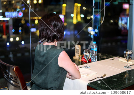 Elegant Woman Enjoying Dinner in a Restaurant with Stunning Night City View Through the Window, Capturing the Essence of Urban Sophistication 139668617
